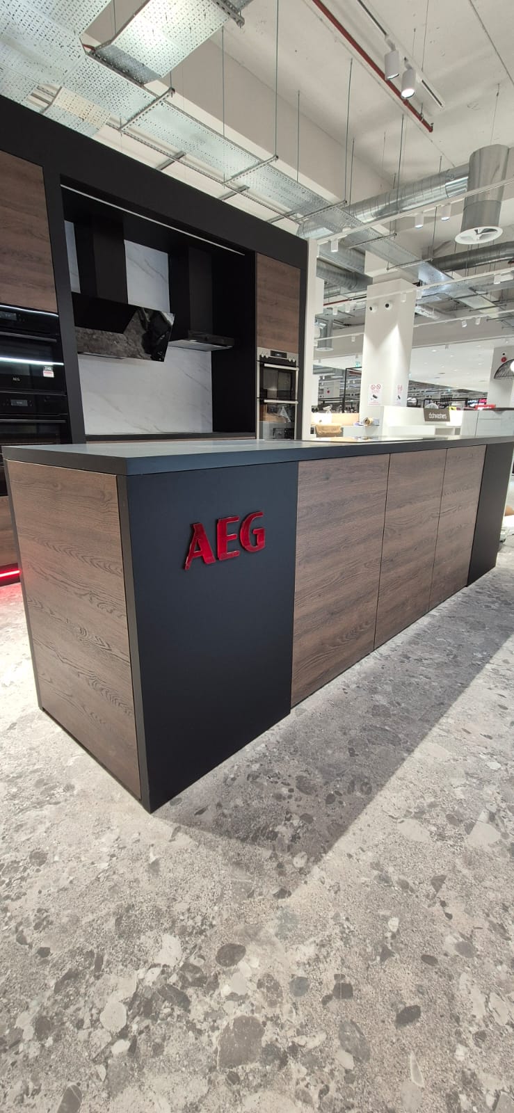 AEG branded shop-in-shop display at Harvey Norman — illuminated header panel and dark wood cabinetry detail
